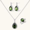 White gold plated jewelry set with green teardrop gemstones and cubic zirconia halos on cream background.