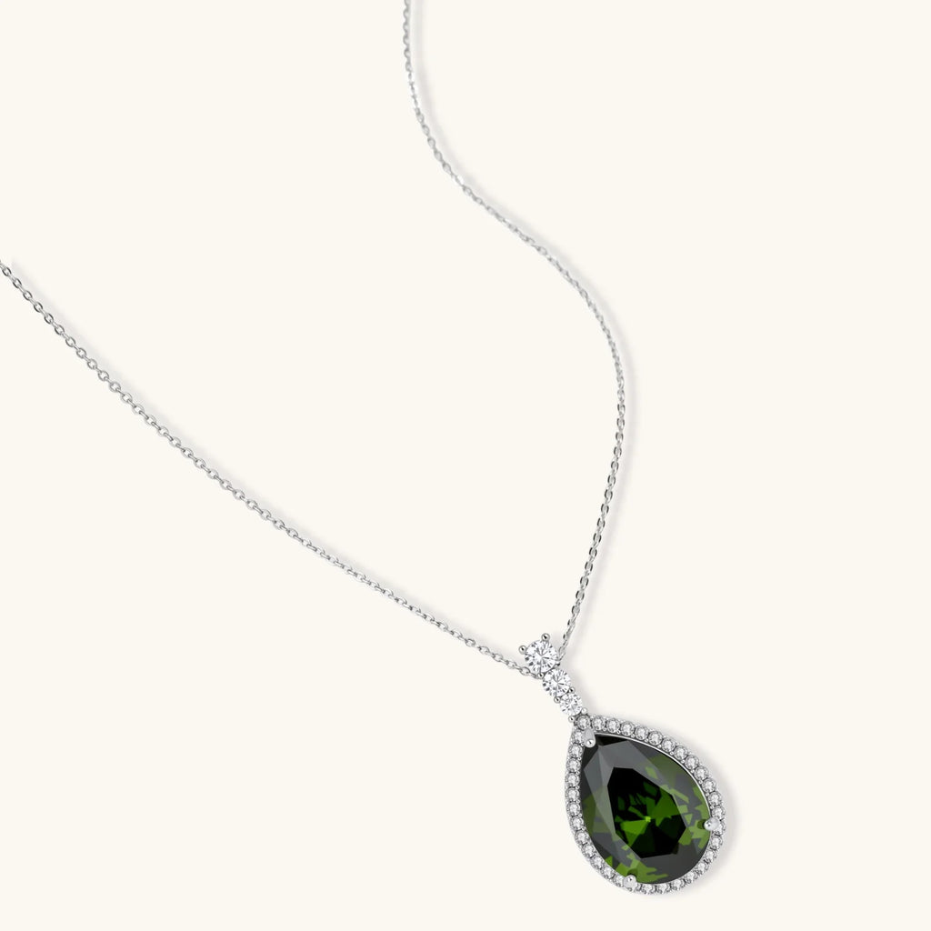 White gold plated jewelry set with green teardrop gemstones and cubic zirconia halos on cream background.