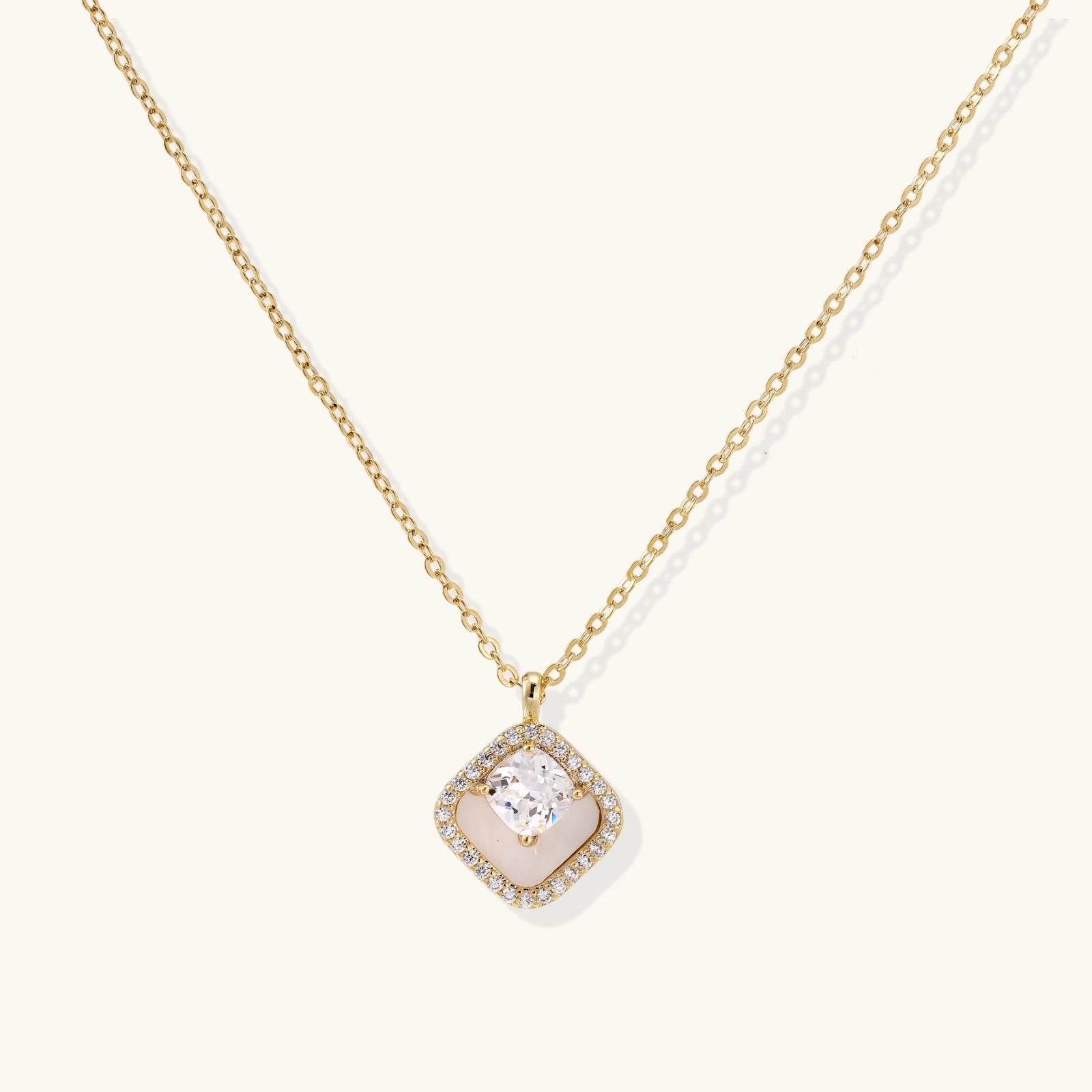 Gold quatrefoil pendant with crystal center on iridescent mother-of-pearl base, adjustable gold chain on cream background