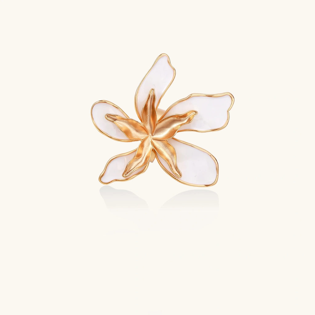 Gold-plated sculptural ring featuring white enamel petals forming an oversized lily bloom on adjustable band