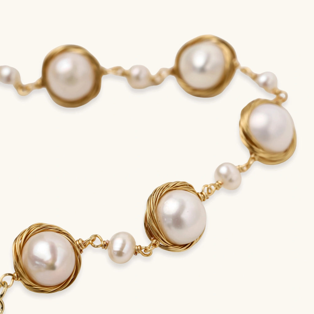 Gold wire-wrapped freshwater pearl bracelet with alternating pearl sizes on cream background, adjustable length